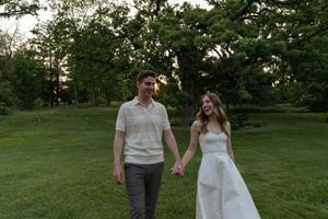Two people in coordinating white and cream outfits walk through a peaceful garden setting.