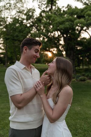 A sweet interaction between two people in white clothing against a natural green backdrop.