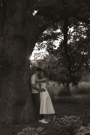 A romantic moment captured against a large tree trunk in moody black and white photography.