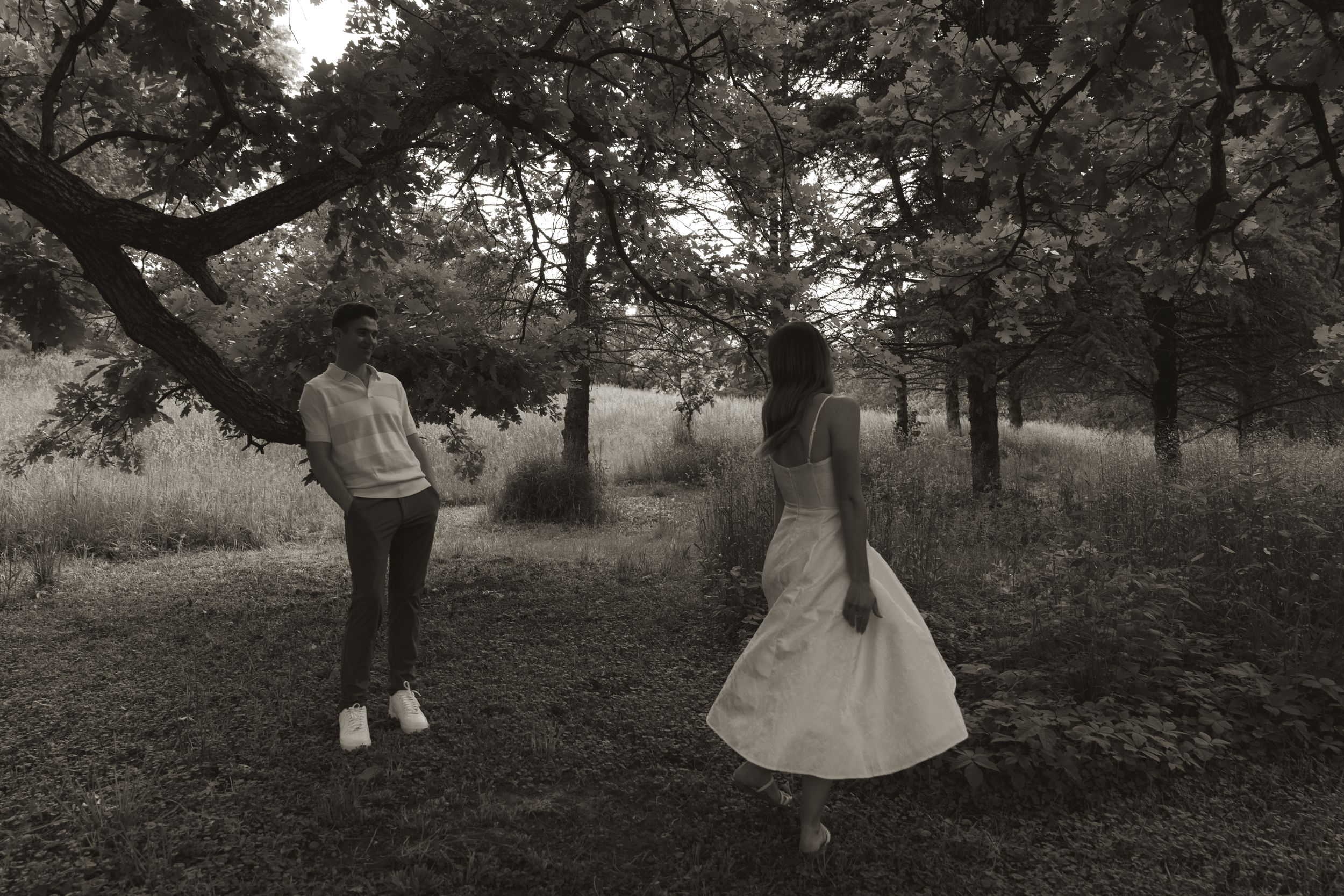 Two figures stand in a serene wooded area captured in black and white photography.