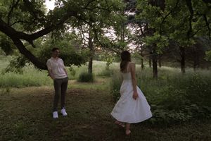 A couple in coordinated white outfits shares a playful moment in a lush green park.