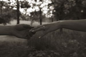 Two hands reach toward each other in a tender moment against a blurred natural background.
