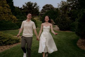 A couple runs joyfully through a park landscape at sunset.