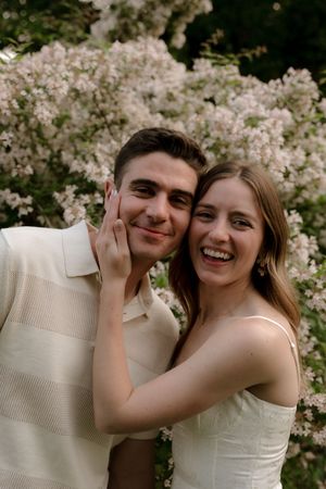 A couple shares a joyful moment together in front of blooming white flowers in a garden setting.