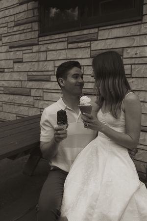 A couple enjoying ice cream cones together against a stone wall in vintage-style photography.