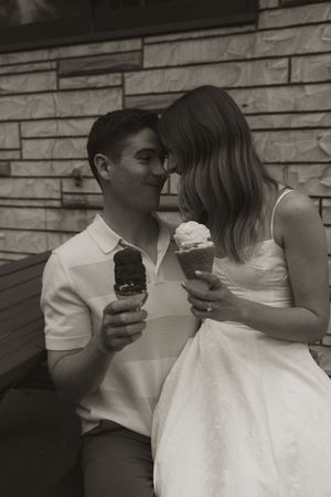 A couple shares a romantic moment while eating ice cream cones against a stone wall background.
