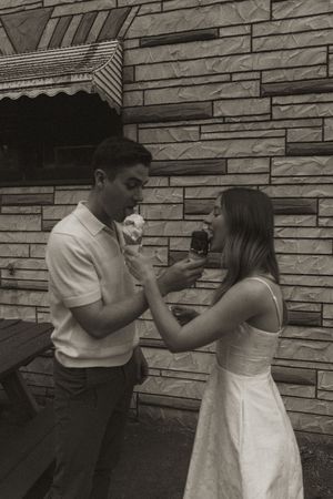Two people playfully feed each other ice cream outdoors on a summer day.