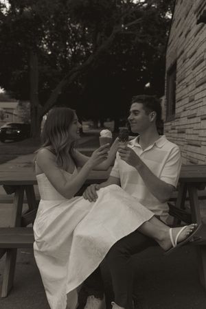 Two people in white outfits share a playful moment with ice cream cones.