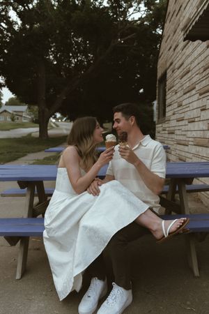 A couple sits on a blue bench sharing ice cream on a summer afternoon.