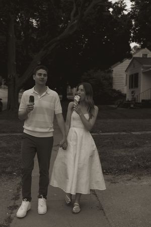 A couple walks together while holding ice cream cones on a summer evening.