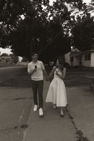 A couple walking together outdoors wearing white and dark colored outfits on a paved path.