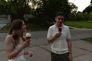 A couple eating ice cream cones while walking together on a path.