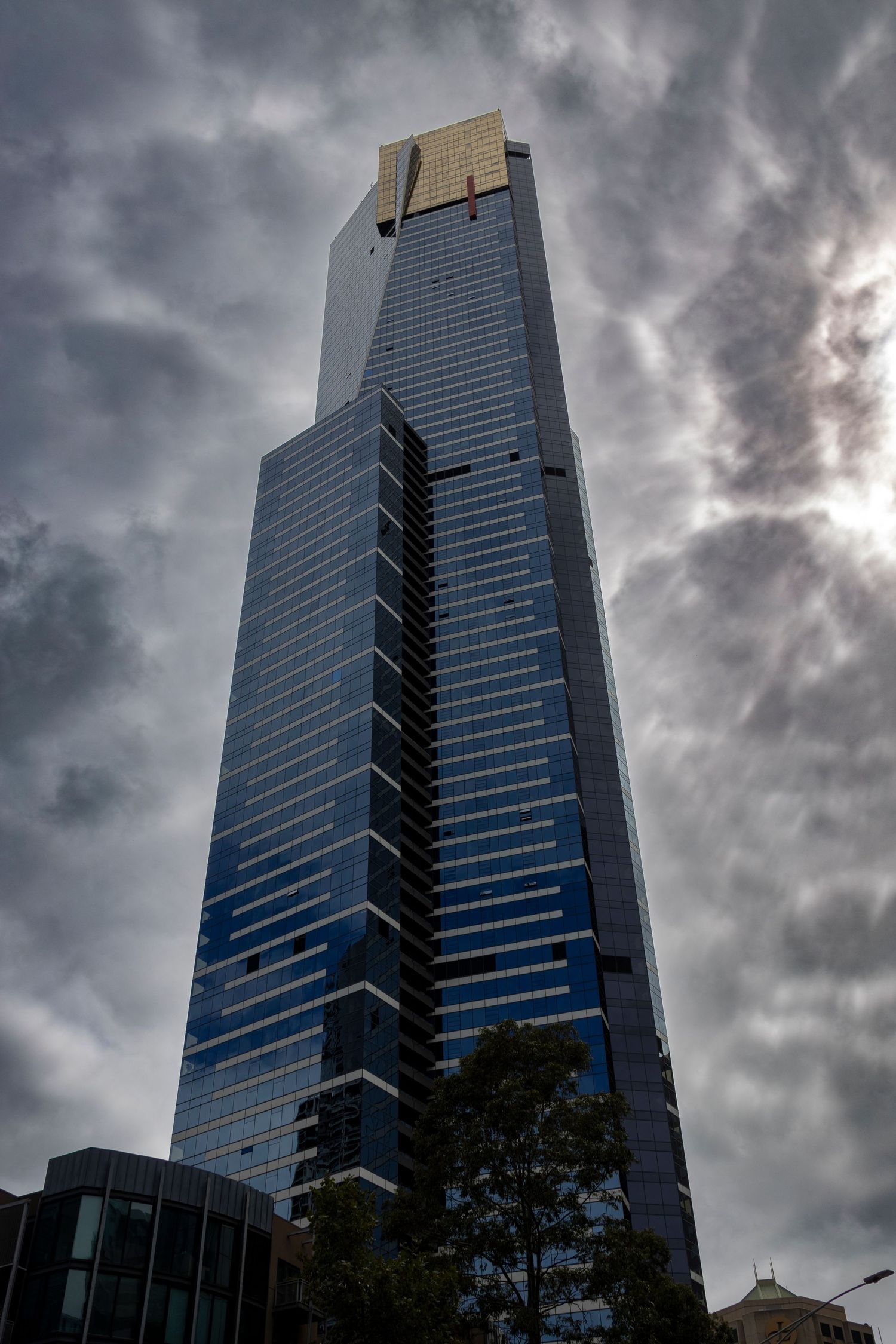Skyscraper piercing the cloudy sky, featuring angular shapes and gold trim near the summit.
