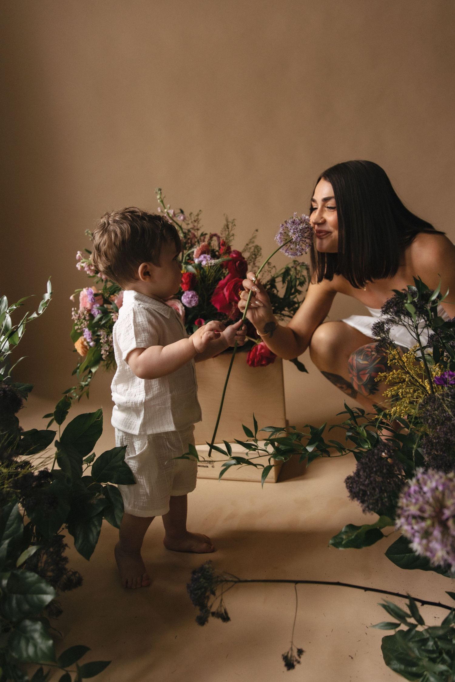 Small child in white clothing explores colorful floral arrangements against a neutral backdrop in a series of connected images.