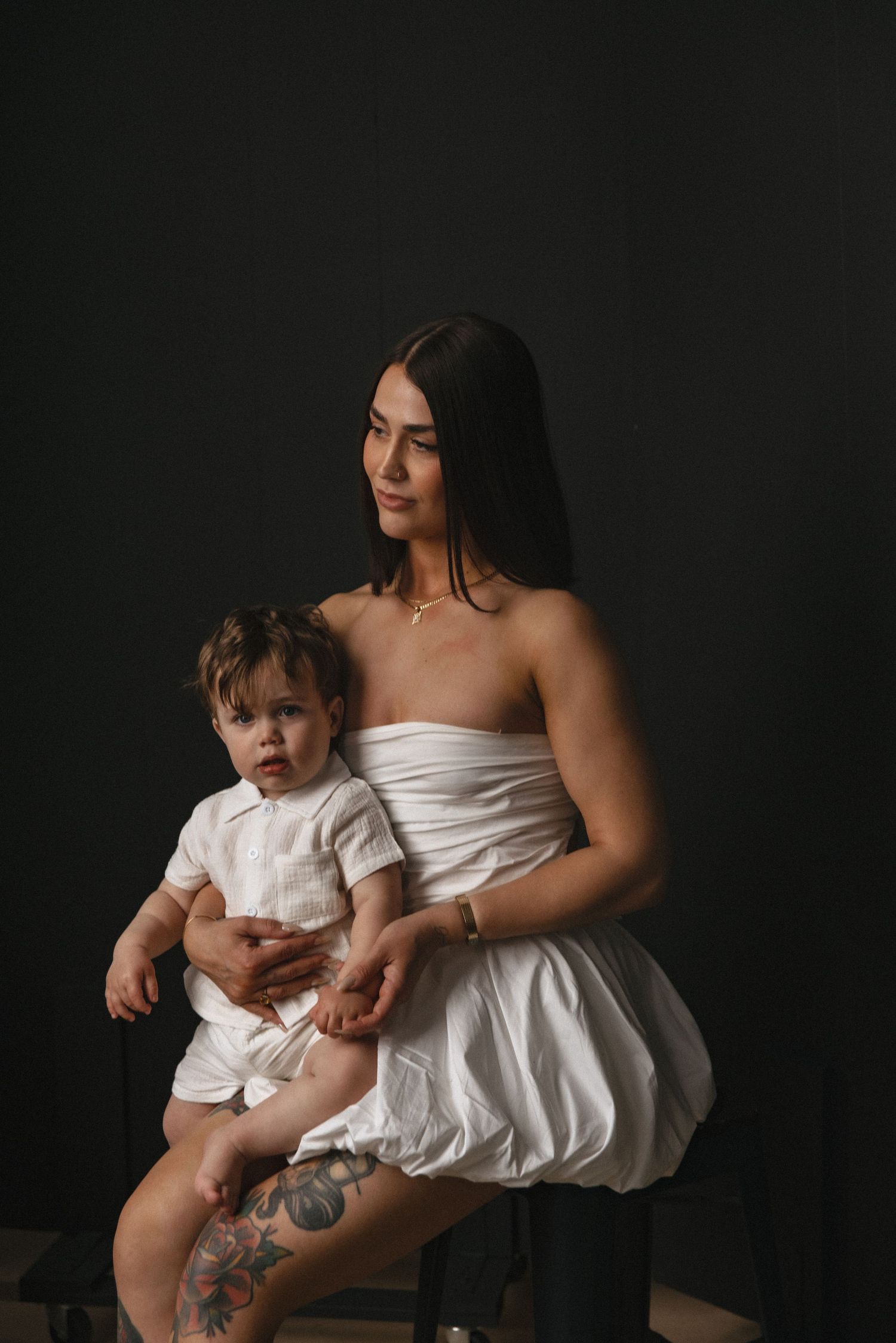 Fine art portrait against dark backdrop with white outfits and soft lighting creating dramatic studio ambiance.
