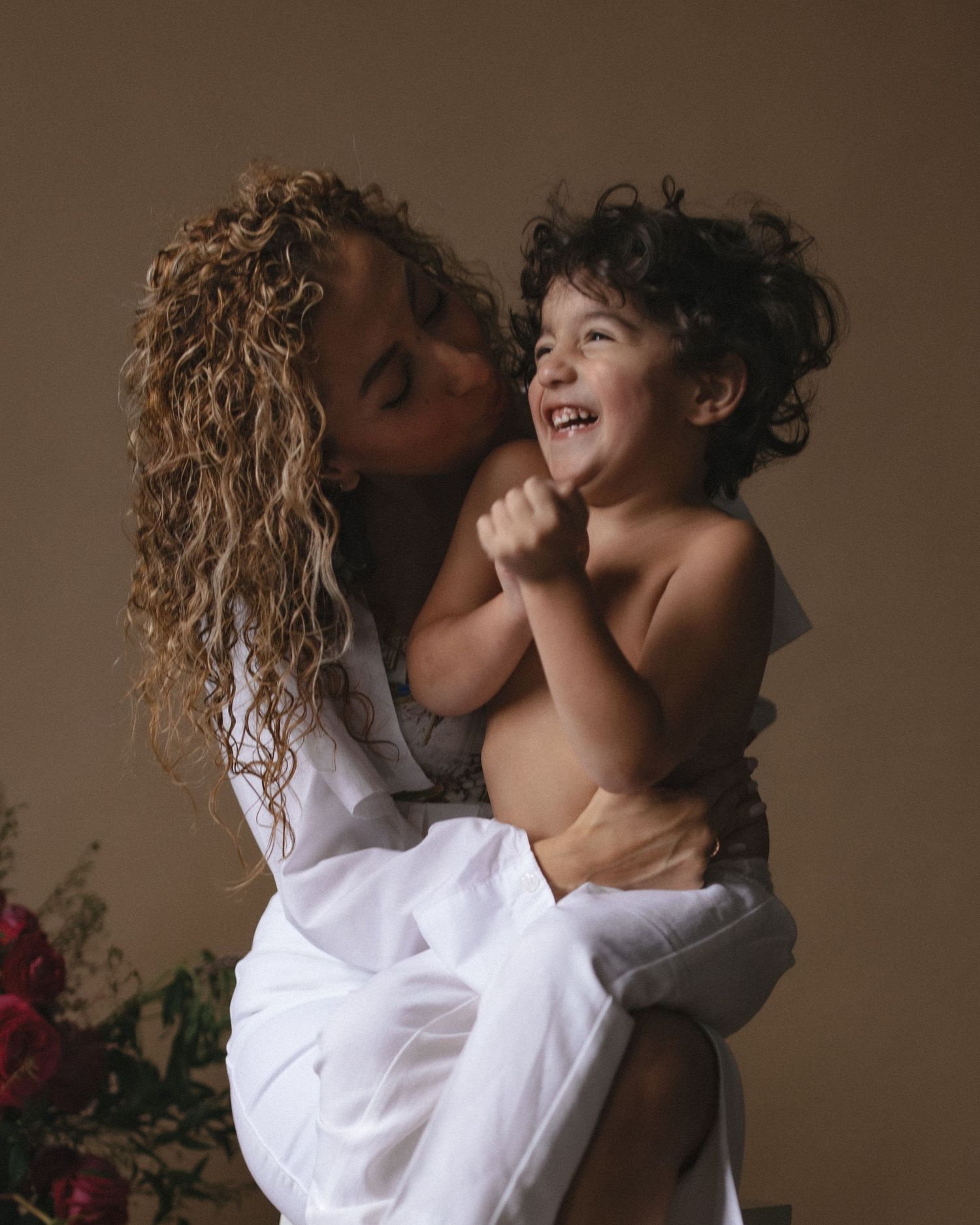 A tender moment captured between parent and child wearing white clothing against a brown backdrop with flowers.