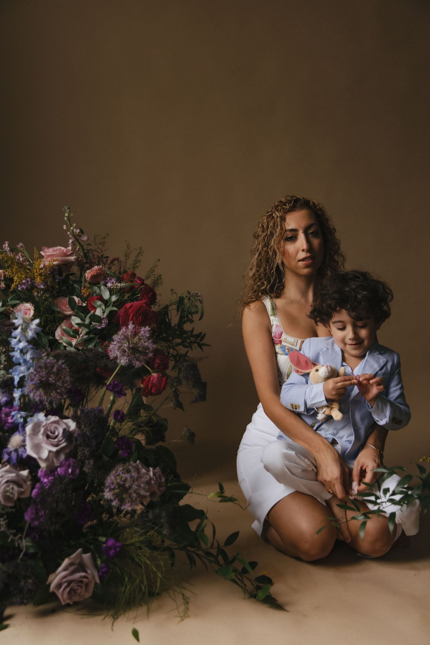 A warm studio portrait with a floral arrangement featuring roses and purple blooms against a brown backdrop.