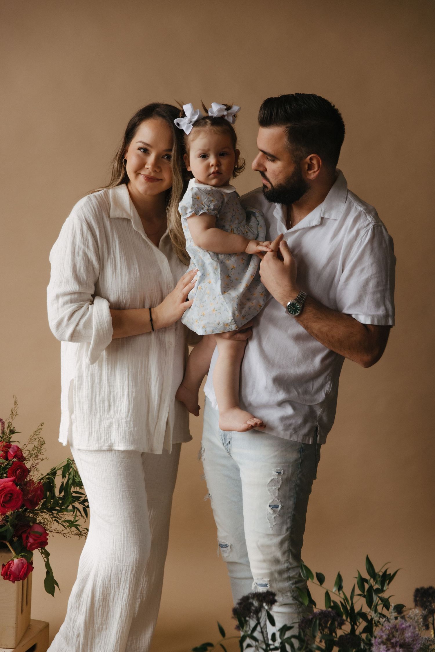 A family portrait in neutral tones with a small child in a gray dress, set against a beige backdrop with red florals.