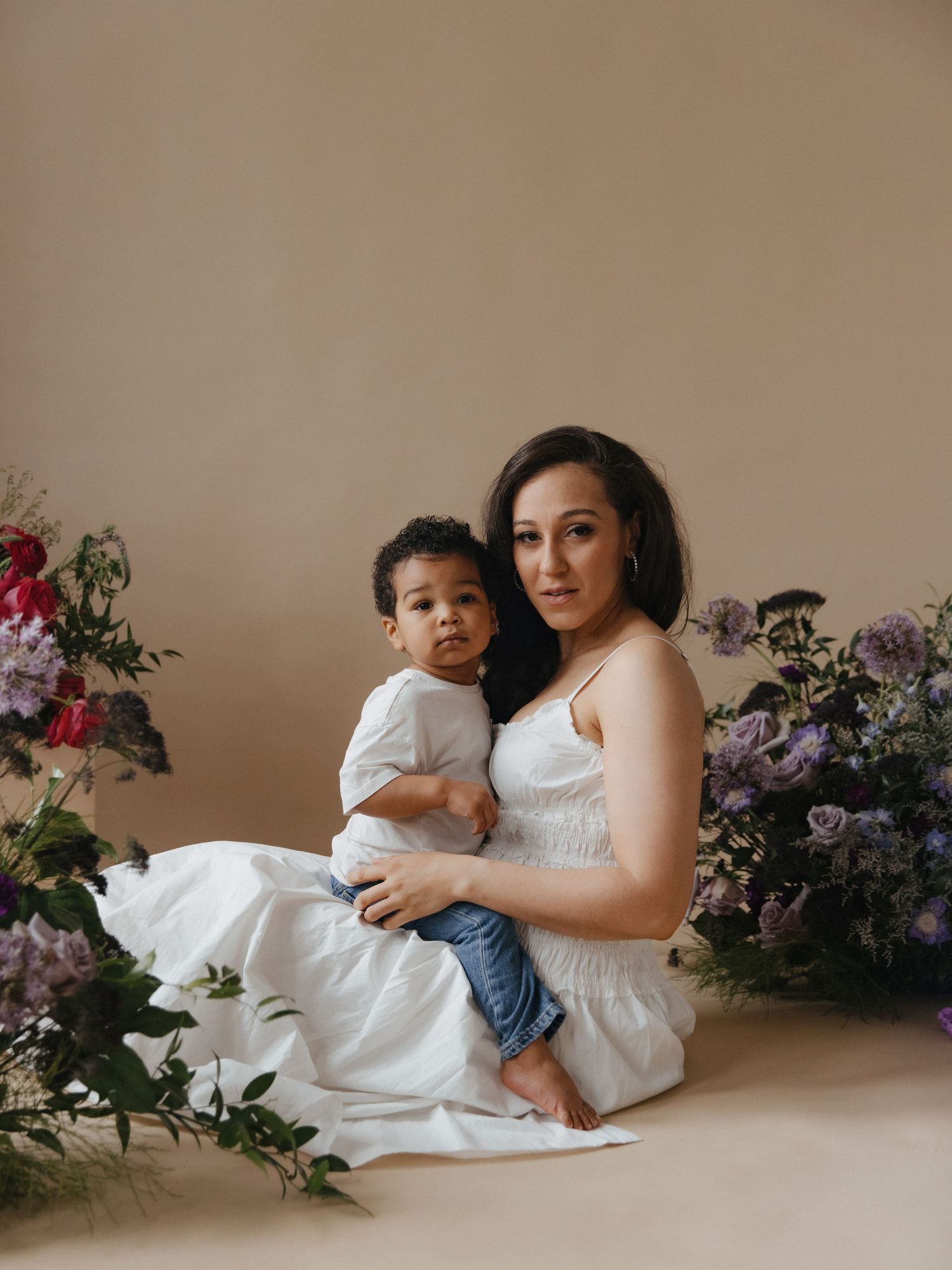 An elegant maternity portrait with beautiful floral arrangements of purple and red blooms framing the serene indoor scene.