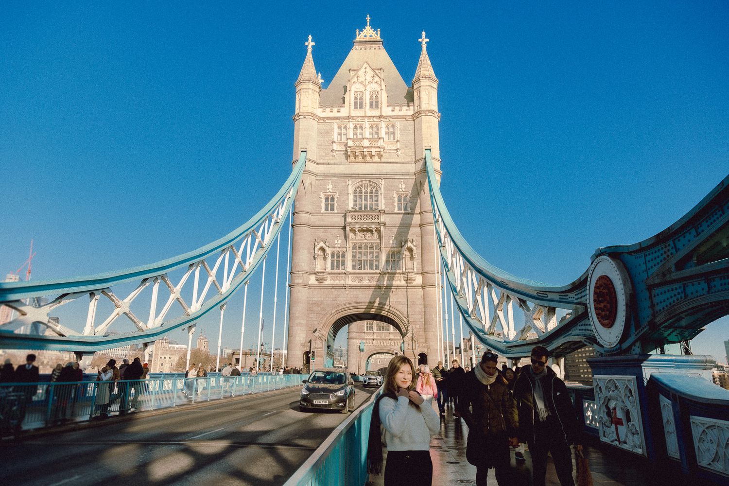 Tower Bridge visitors walking across the famous London landmark on clear sunny afternoon.