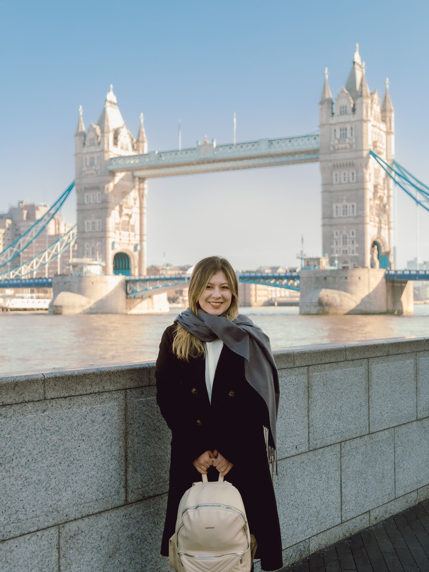 Tourist with beige backpack poses in front of London's historic Tower Bridge.