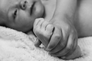 Close-up black and white photo of two hands tenderly clasped together against white fabric.