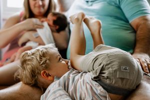 Young child with blonde hair laying on couch with family enjoying casual relaxed time together at home.