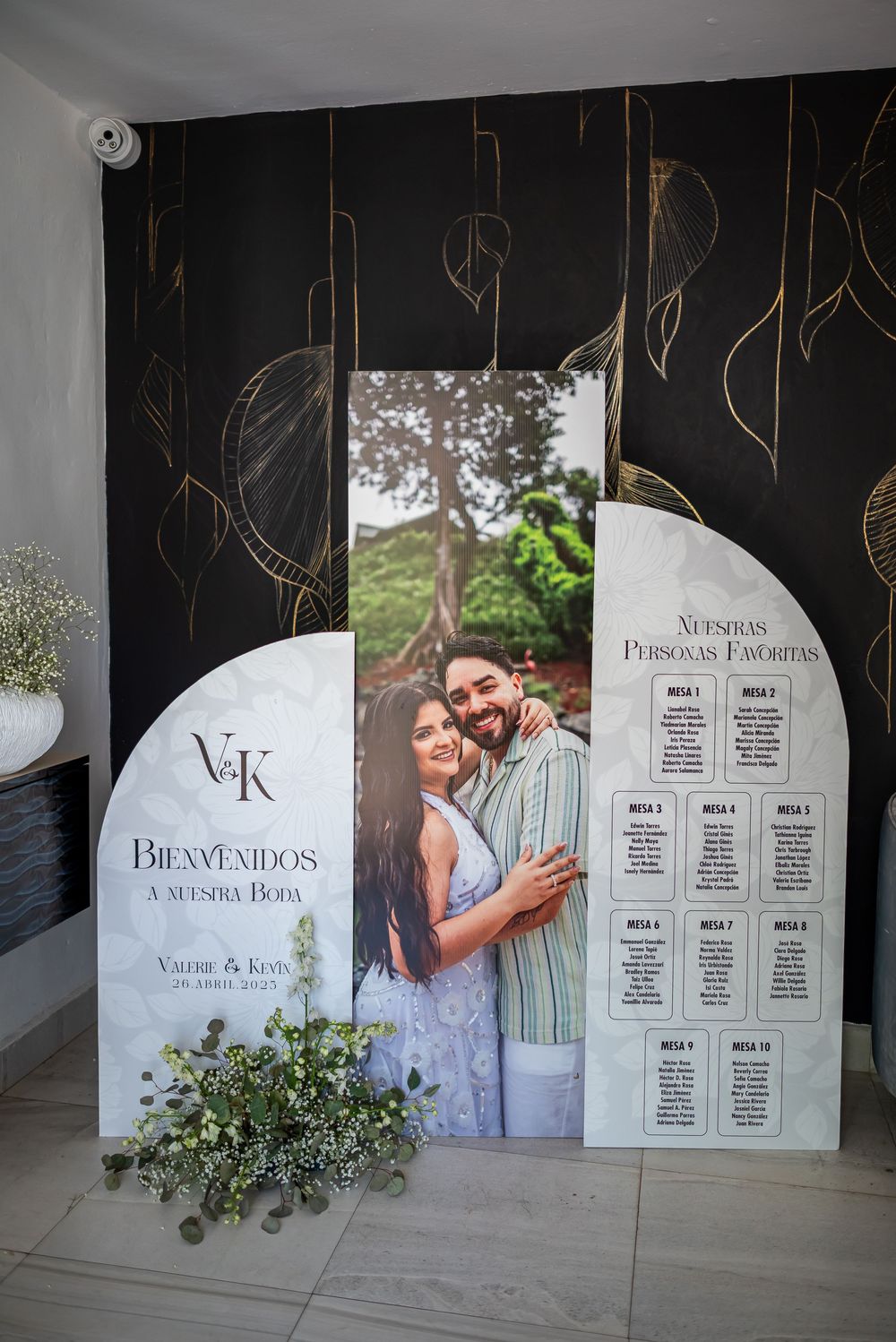 Wedding seating chart display with welcome sign and decor featuring elegant black panels with gold leaf design.