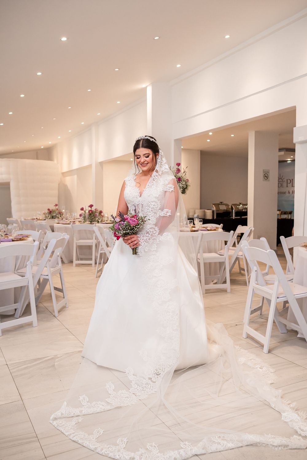 A stunning bridal portrait in a white wedding dress with long lace train and bouquet in an elegant reception venue.
