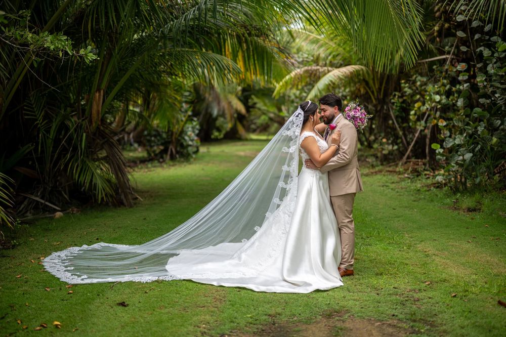 A wedding couple embraces in a lush tropical garden setting with a long flowing white veil trailing behind the bride.