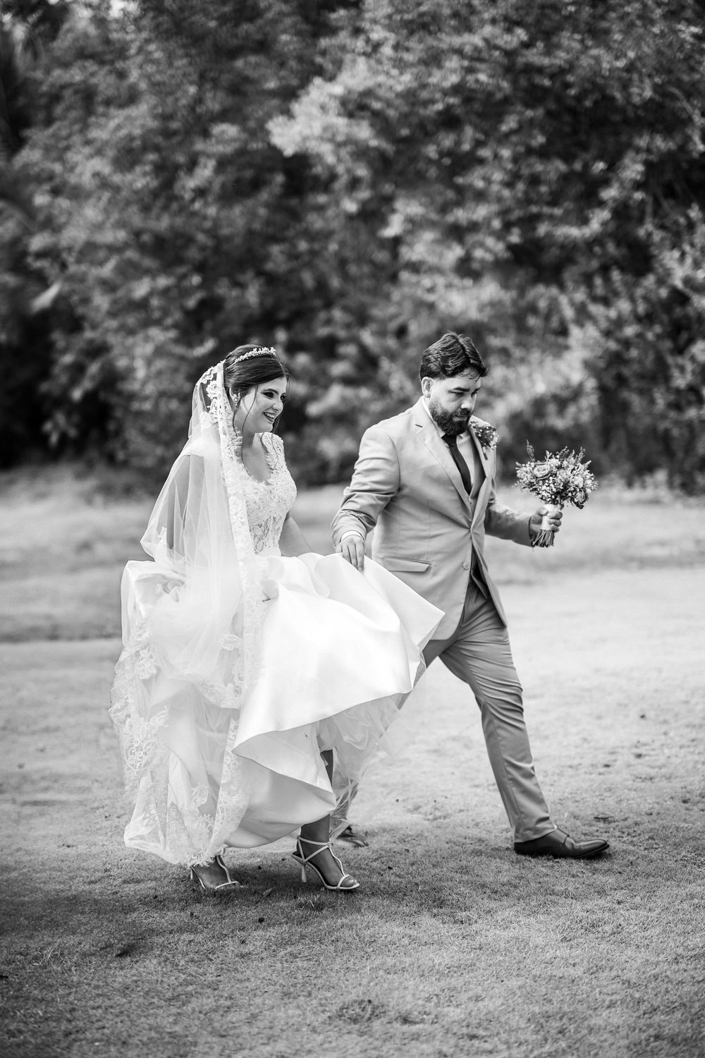 Black and white wedding photo capturing candid movement as couple walks together outdoors.