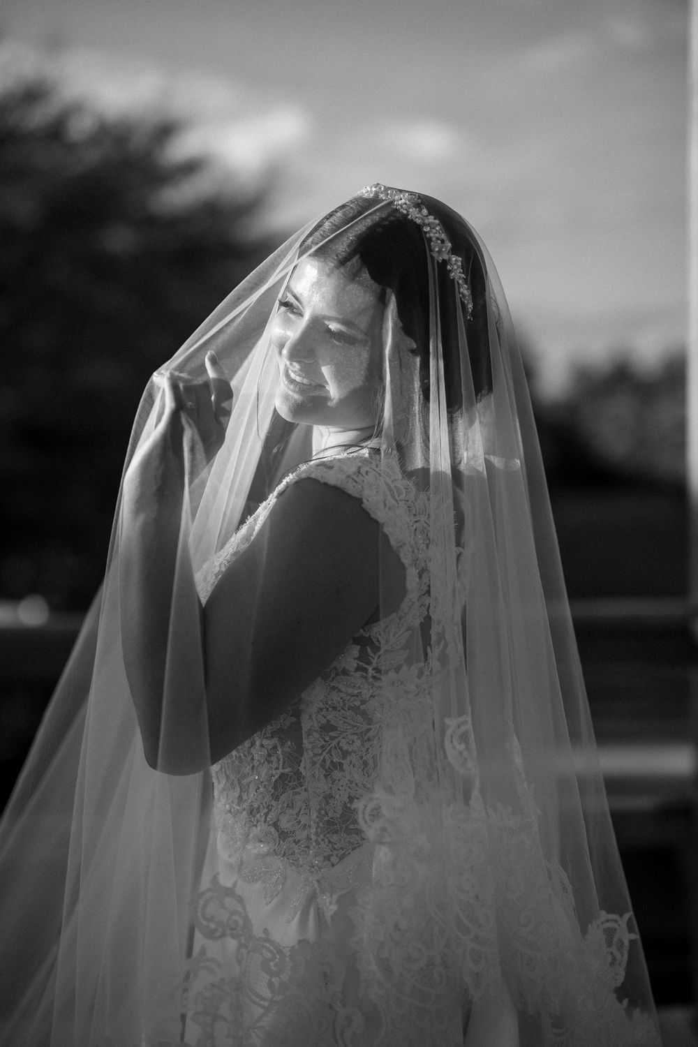 An artistic black and white portrait of a bride wearing a delicate lace veil.