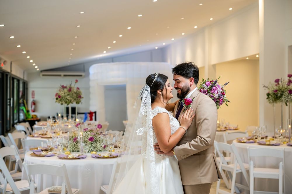 A tender moment between newlyweds in a wedding reception venue decorated with floral centerpieces and white chairs.