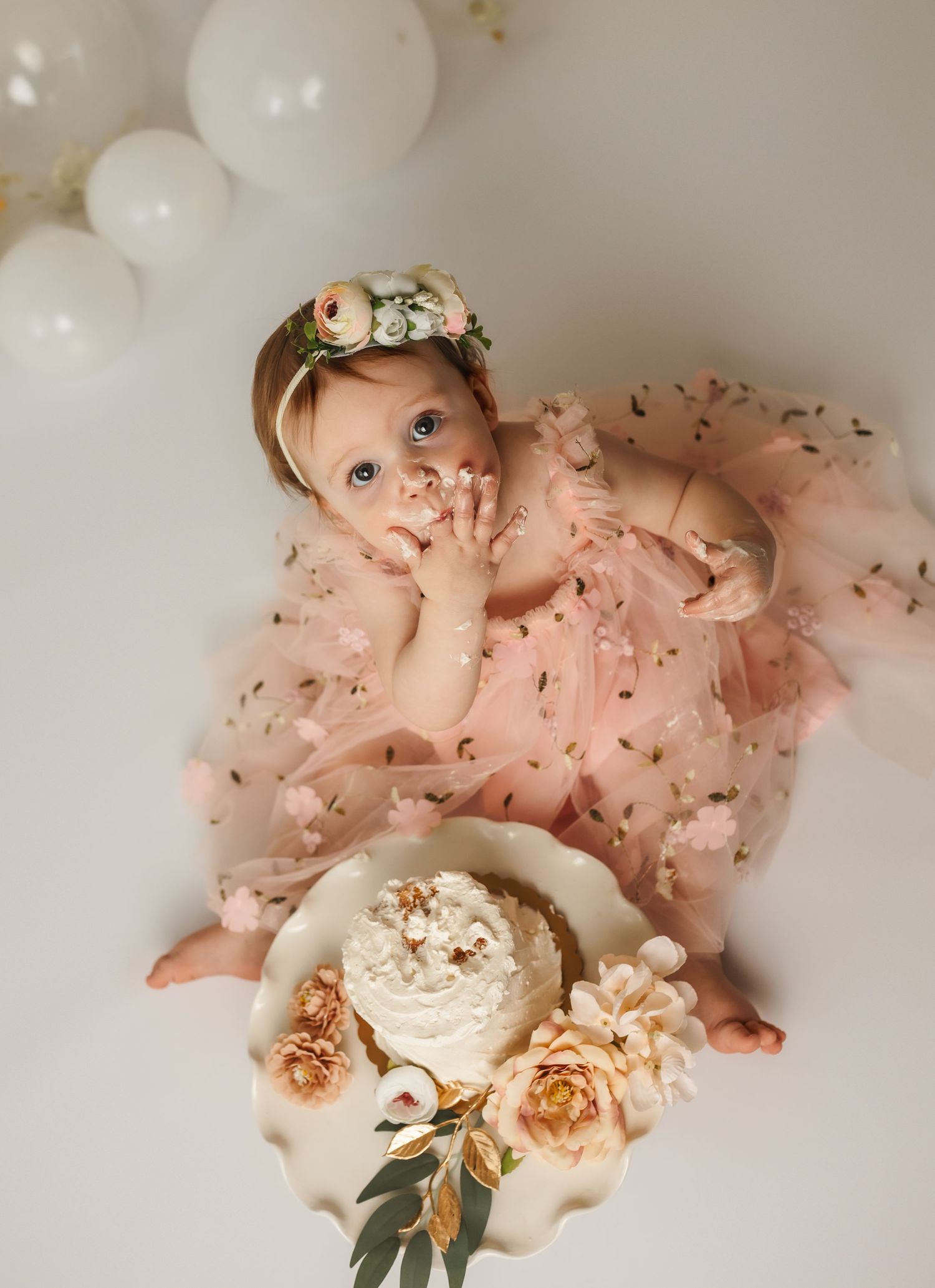 Overhead shot of a baby girl in a pink tulle dress smashing a cake decorated with roses during a Charlottesville studio cake smash session.