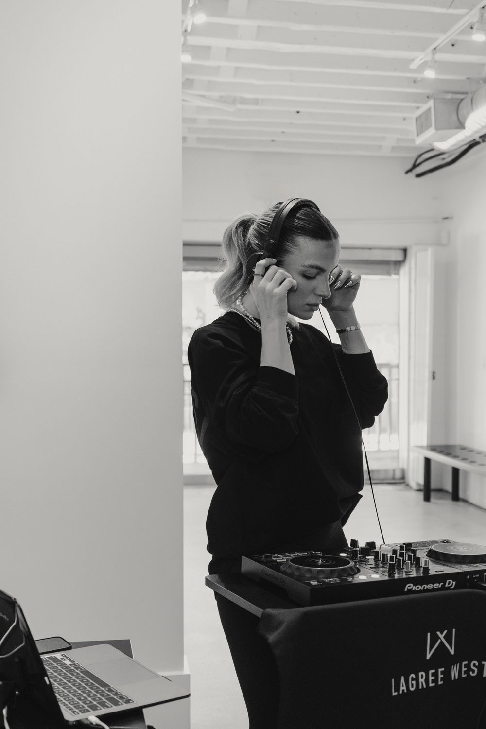 DJ at work using audio equipment in a bright minimalist studio space while wearing dark clothing.