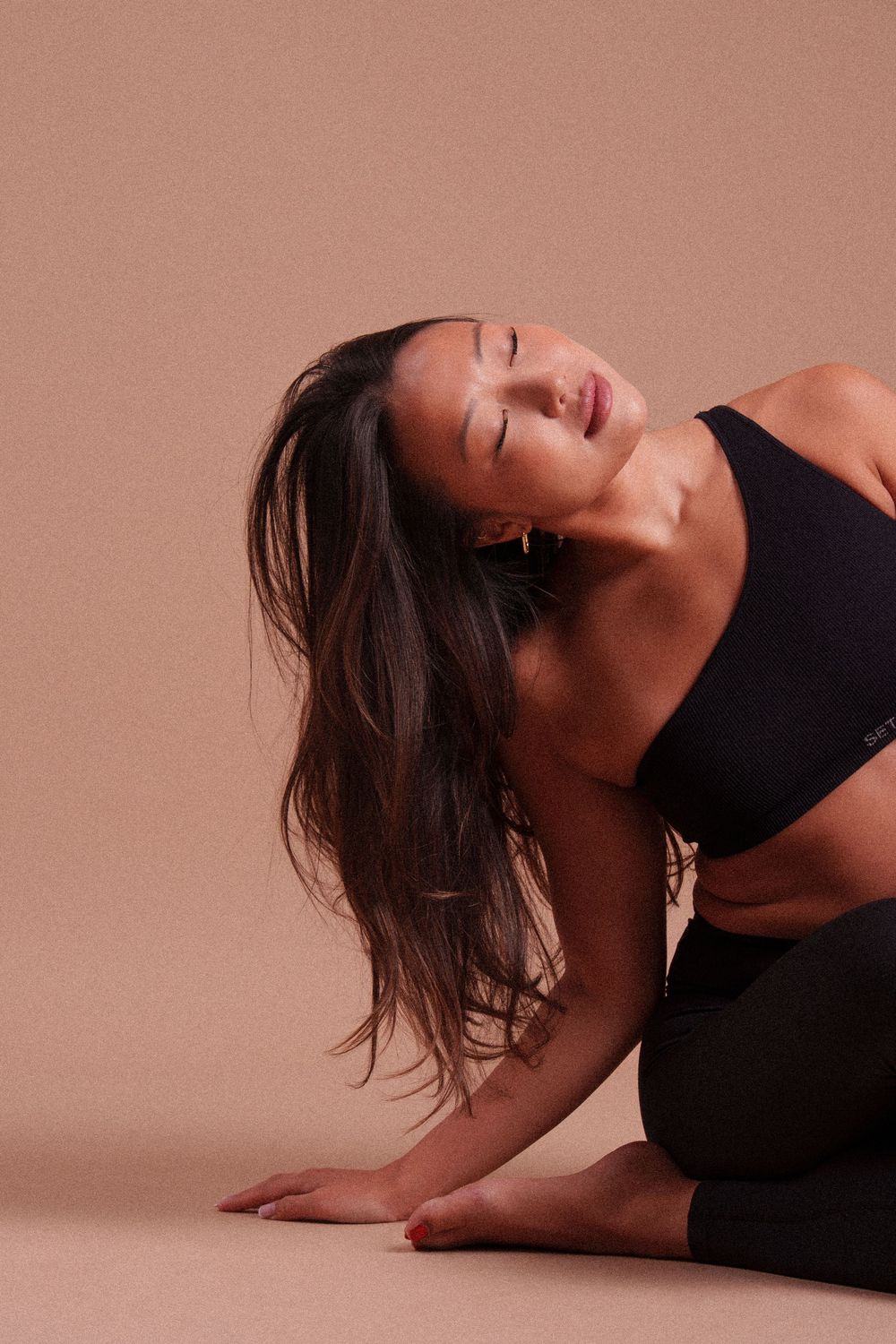 Athletic figure in black workout attire strikes graceful dance pose against dusty rose backdrop.