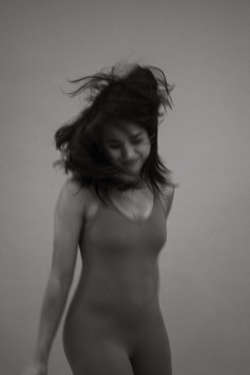 Black and white artistic photo of a dancer in a leotard with windswept hair against a plain backdrop.