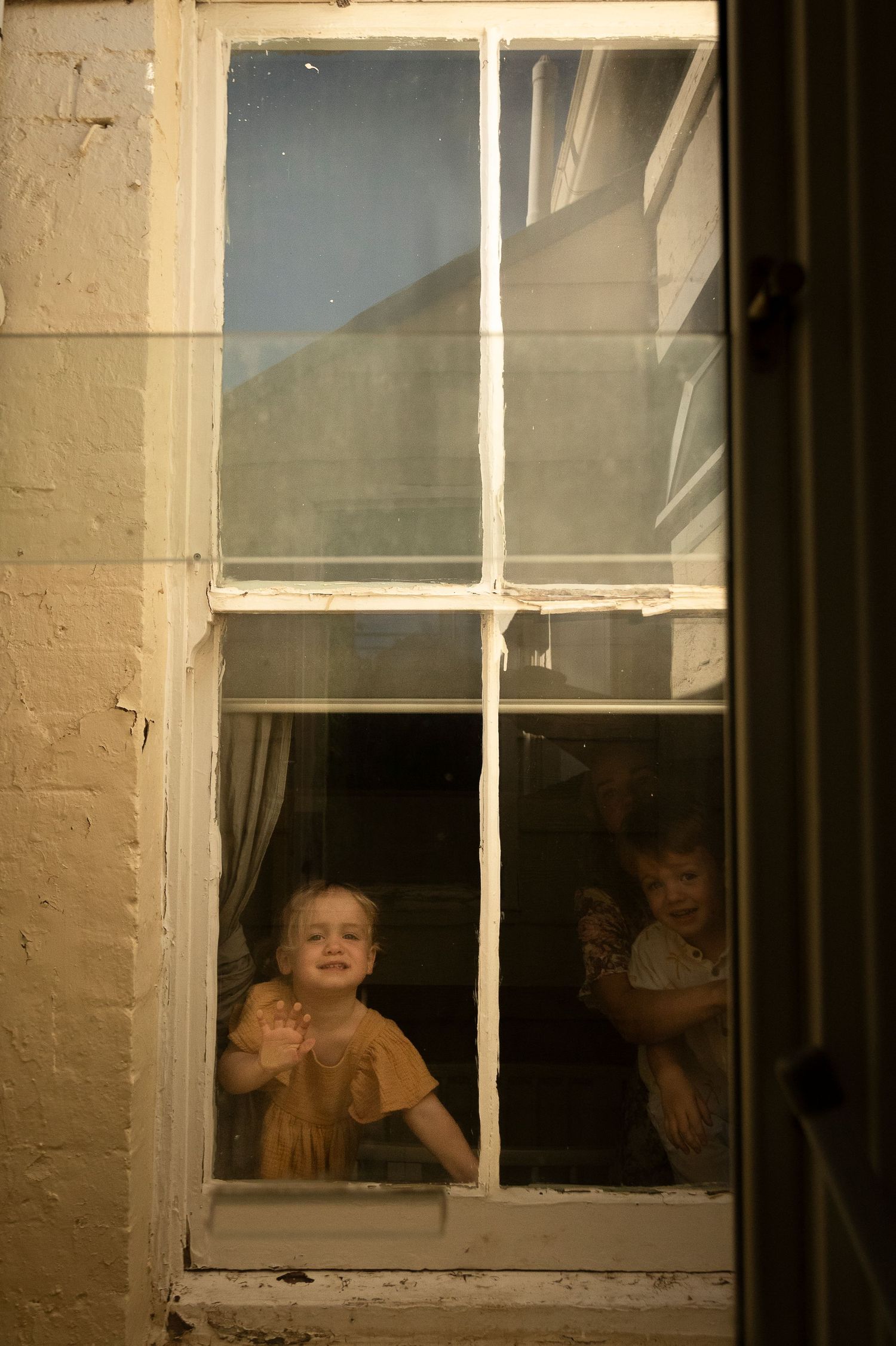 Children peering playfully through a series of white-framed windows against a light colored wall.