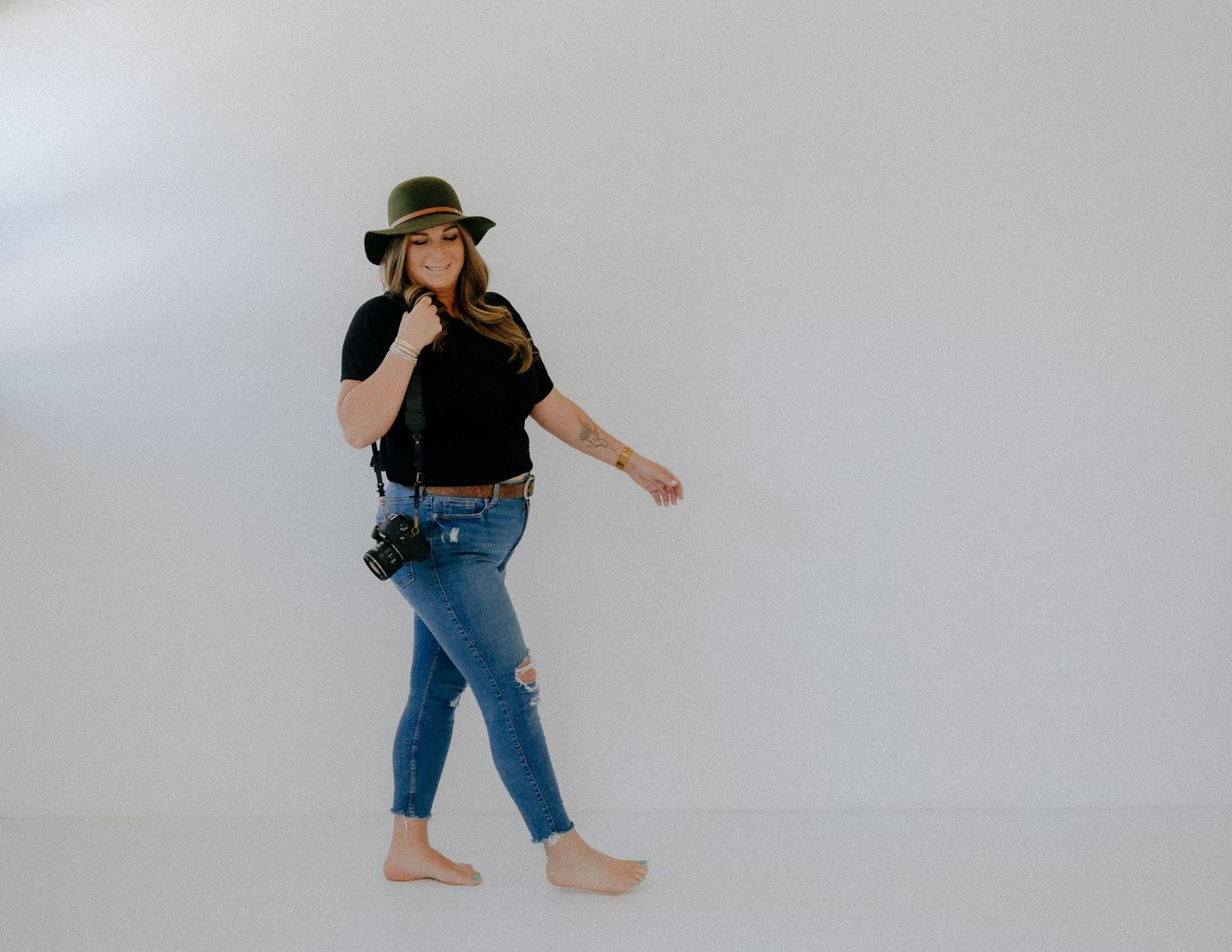 Casual figure in denim and hat dancing barefoot against white backdrop.