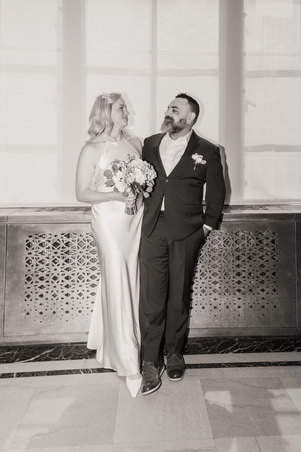 Black and white photo of a bride in a white gown holding a bouquet and groom in a dark suit at their wedding.