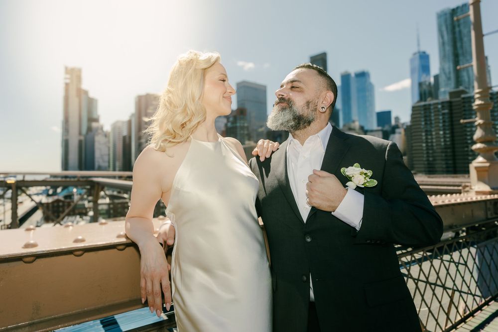 Bride and groom share a romantic moment on a bridge with NYC skyline backdrop on their wedding day.