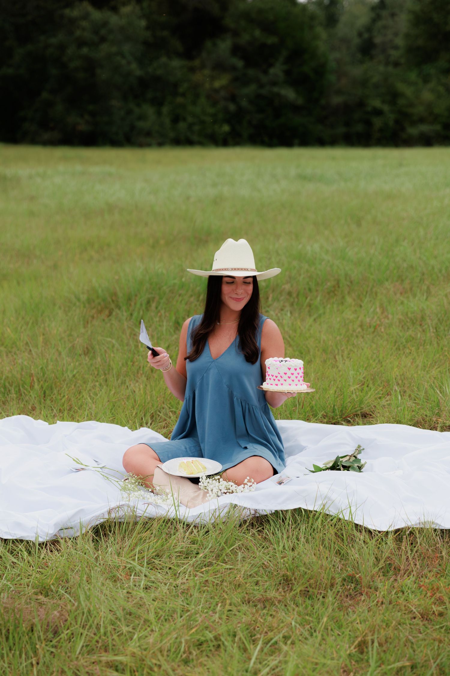 Woman in blue dress having picnic with cake in grassy field.