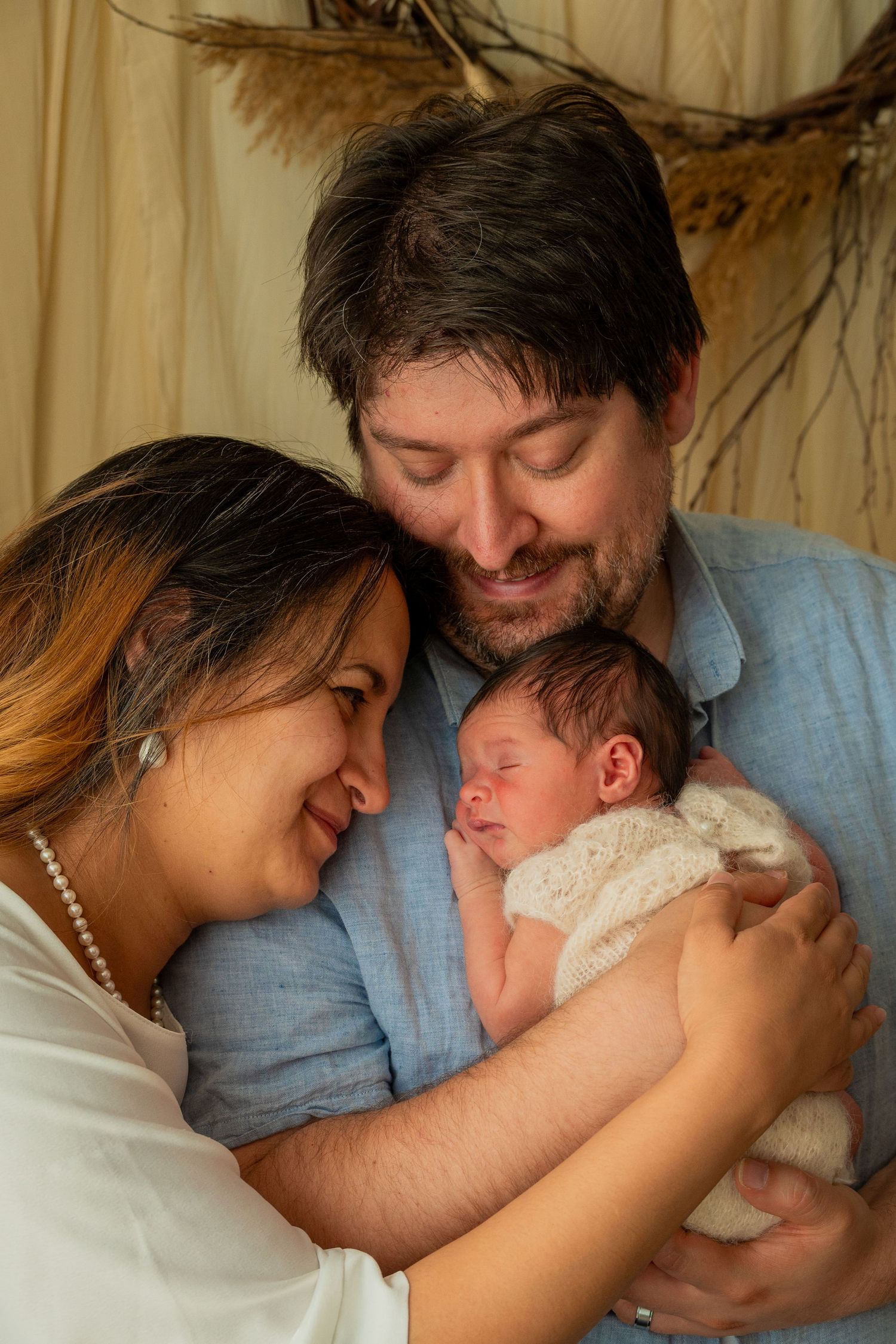 Tender family moment with newborn baby being cradled by parents in warm lighting.