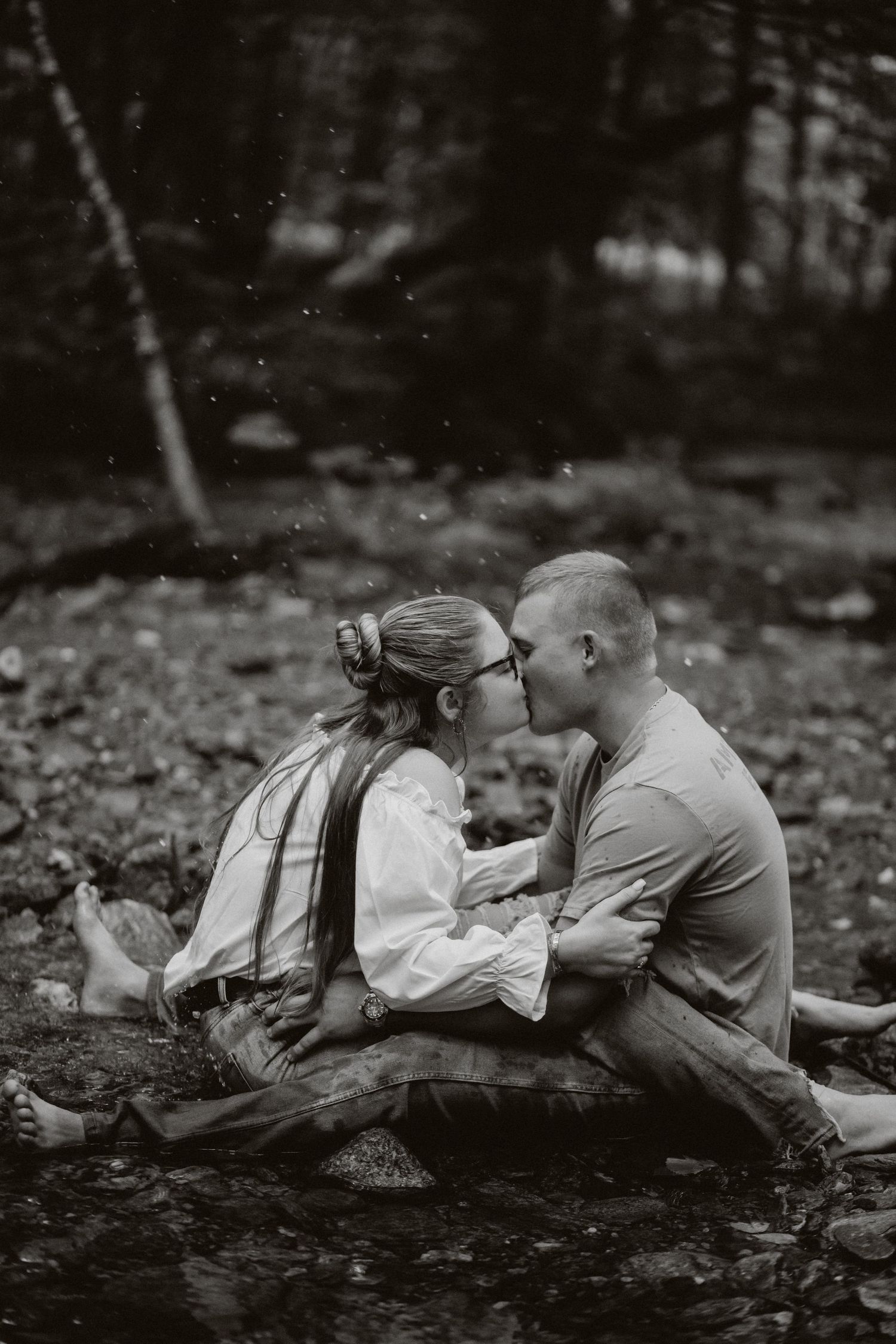 An intimate black and white photo of a couple sharing a tender moment by a stream.