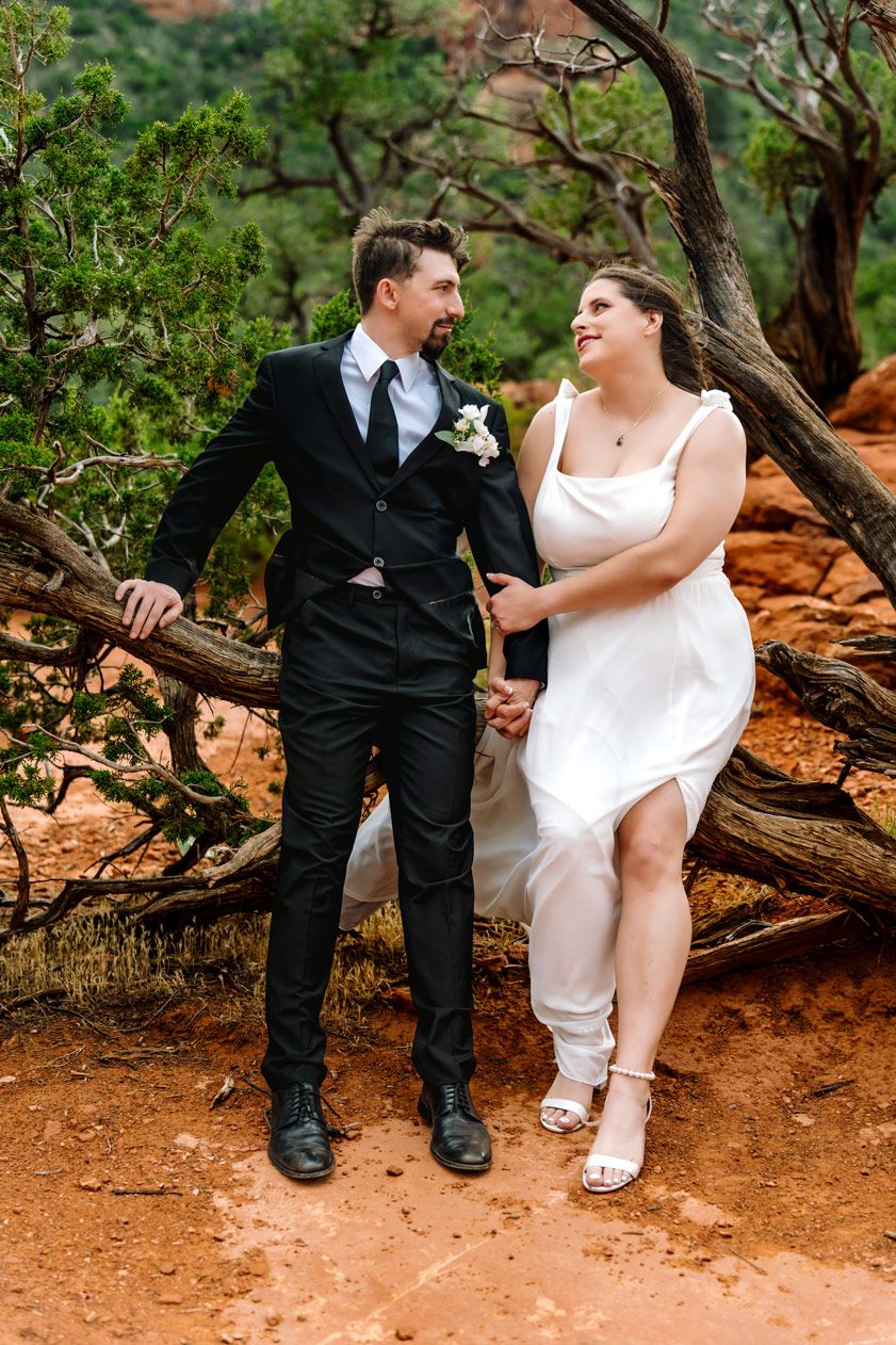 A romantic wedding couple poses together on Sedona red rocks surrounded by desert brush.