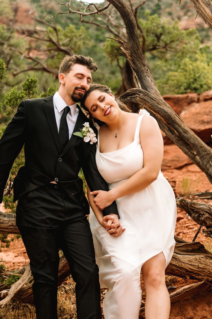 Joyful wedding couple sharing a laugh on Sedona red rocks in a desert landscape.