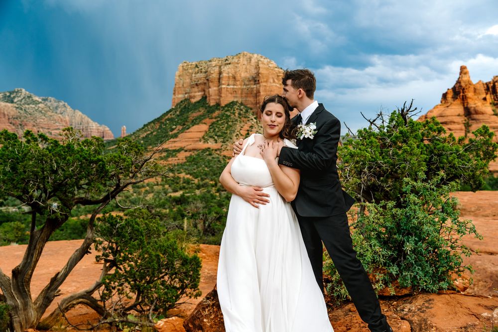 A wedding couple embraces against Sedona's iconic red rock formations and blue sky backdrop.