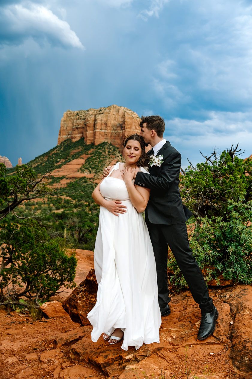 A romantic wedding portrait with dramatic red rock formations and stormy skies in Sedona.