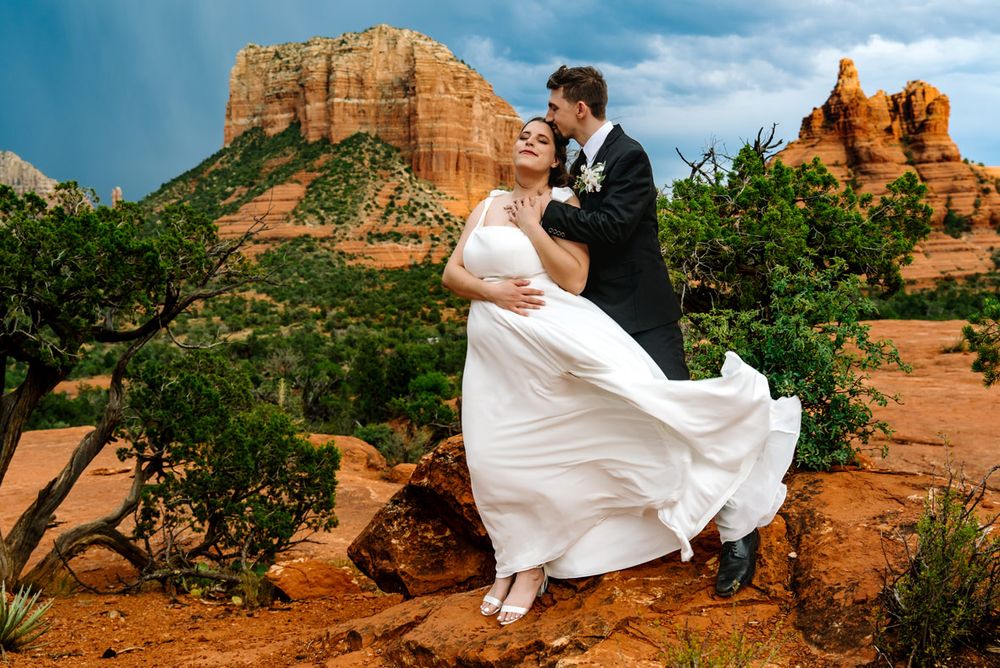 A flowing white wedding dress catches the wind against Sedona's majestic red rock landscape.