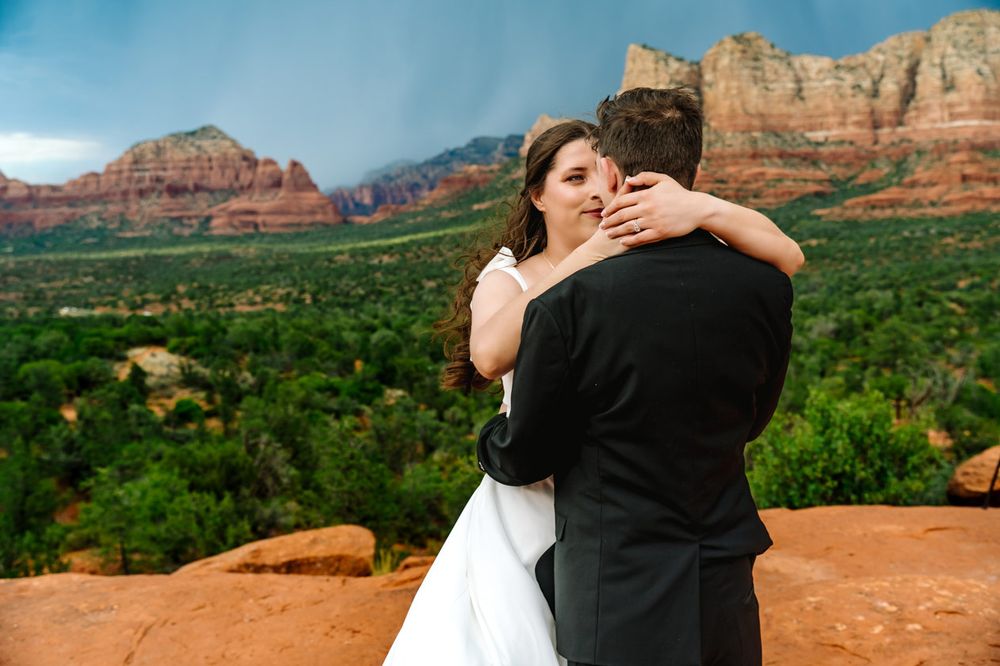 Wedding couple shares an intimate embrace on red rocks overlooking Sedona's valley.